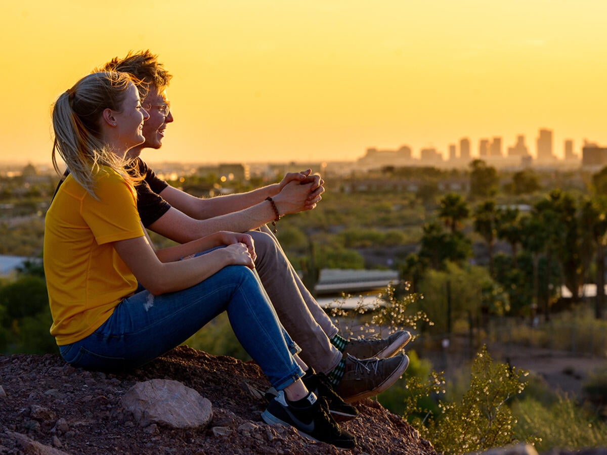 Two students sitting on a hillside overlooking campus